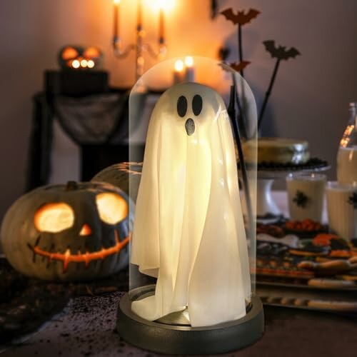 Halloween ghost decoration under a glass dome with pumpkins and candles.